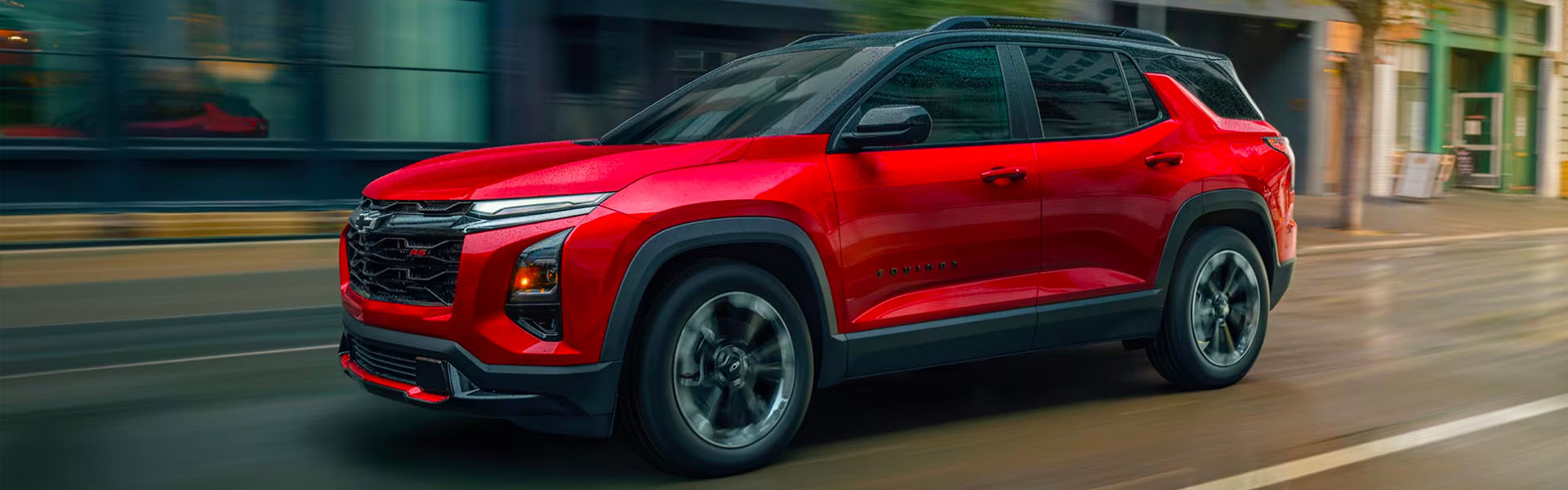 2026 Chevrolet Equinox compact SUV in red driving through an urban city street, featuring sporty exterior styling and everyday versatility.