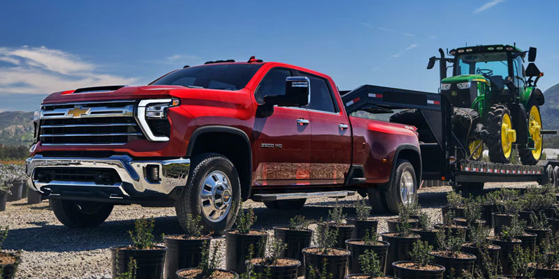 Chevrolet Silverado 2500HD towing a large tractor on a rural road, showcasing its powerful towing capability.